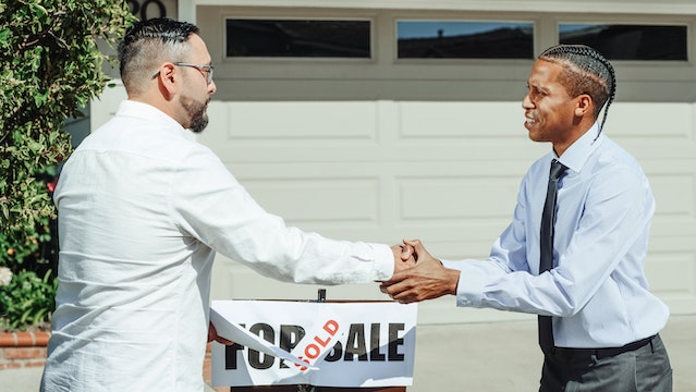 people shaking hands in front of a sold sign